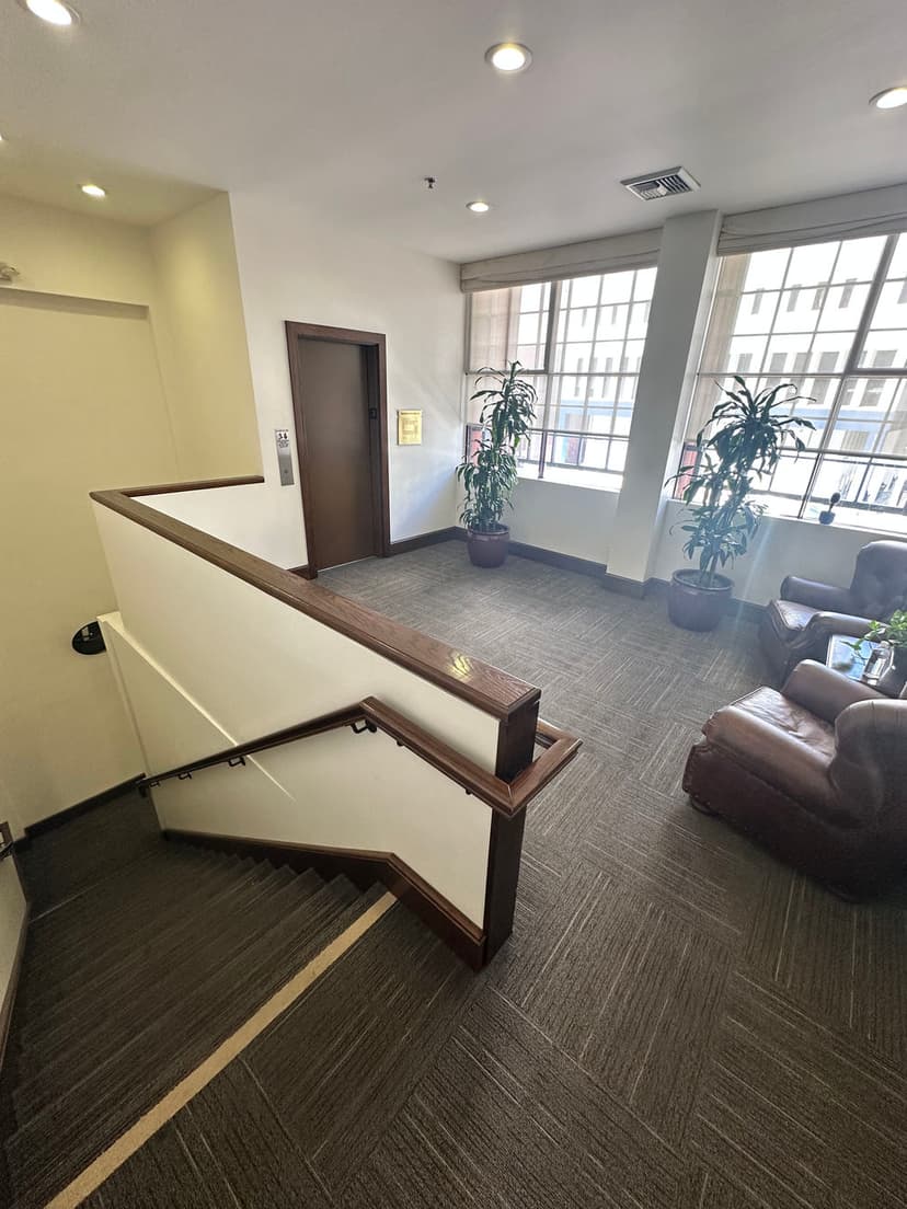 Interior stairwell with wooden railing, plants, and seating area in a bright, inviting space.