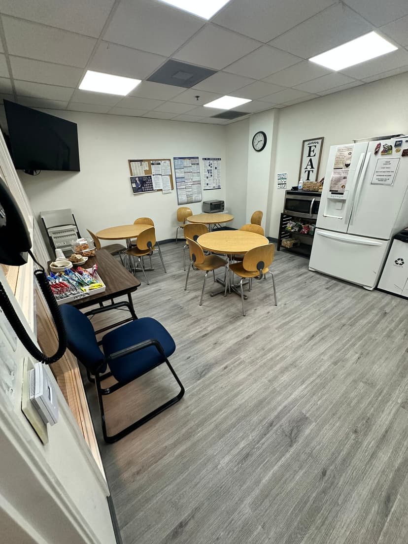 Break room with tables, chairs, fridge, clock, and bulletin board for employee use.